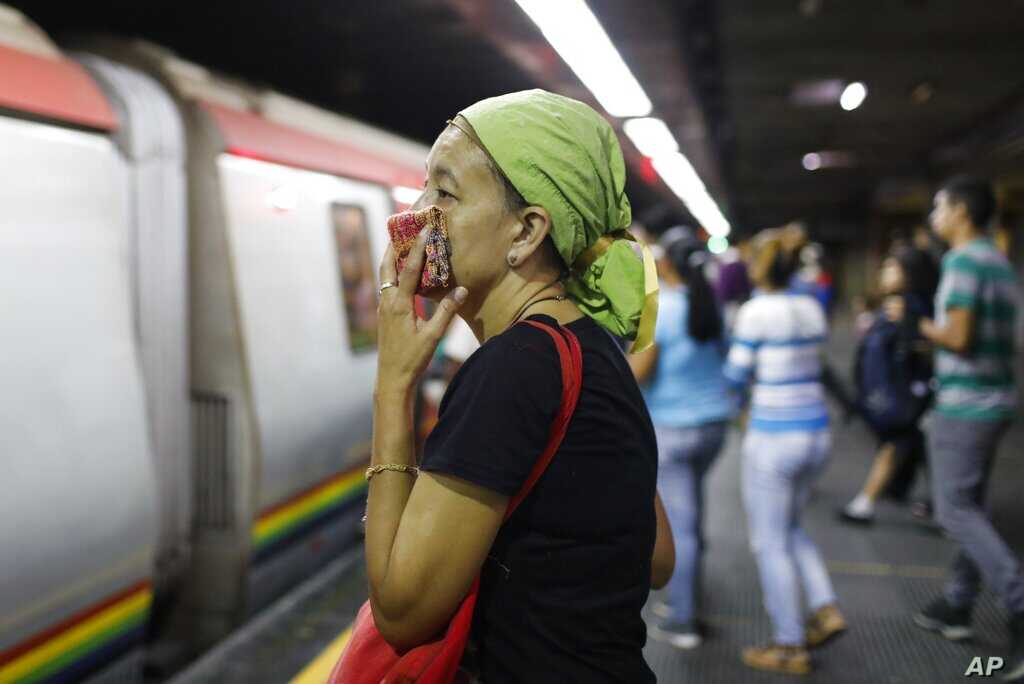 A woman covers her mouth and nose with a wash cloth on a subway platform in Caracas, Venezuela, Friday, March 13, 2020. Venezuela's Vice President Delcy Rodríguez confirmed Friday the first two cases of the new coronavirus in the South American country. The vast majority of people recover from the new virus. (AP Photo/Ariana Cubillos)